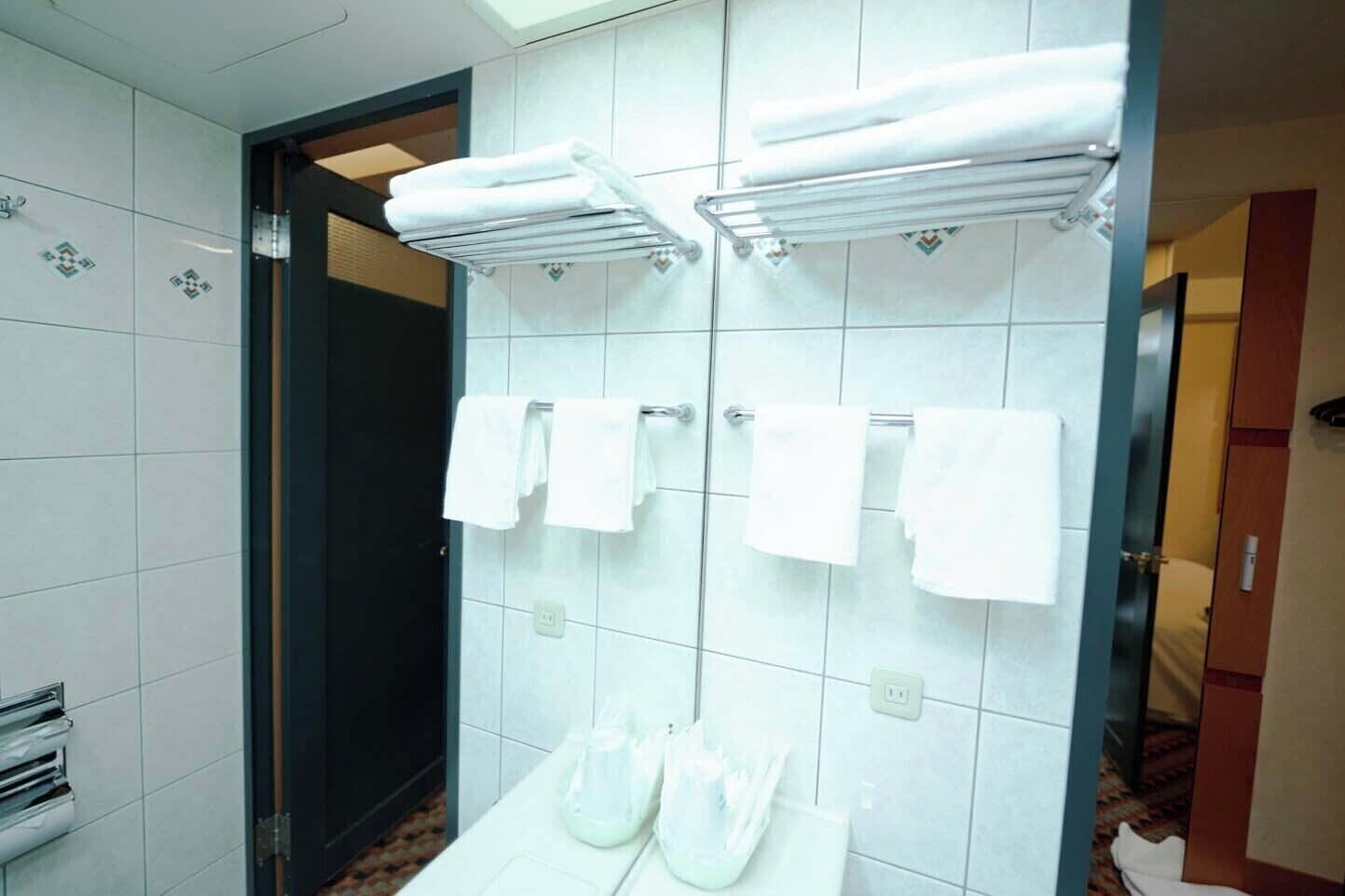 A bathroom with white tiled walls, a shower area, and a toilet with a glass shower enclosure.