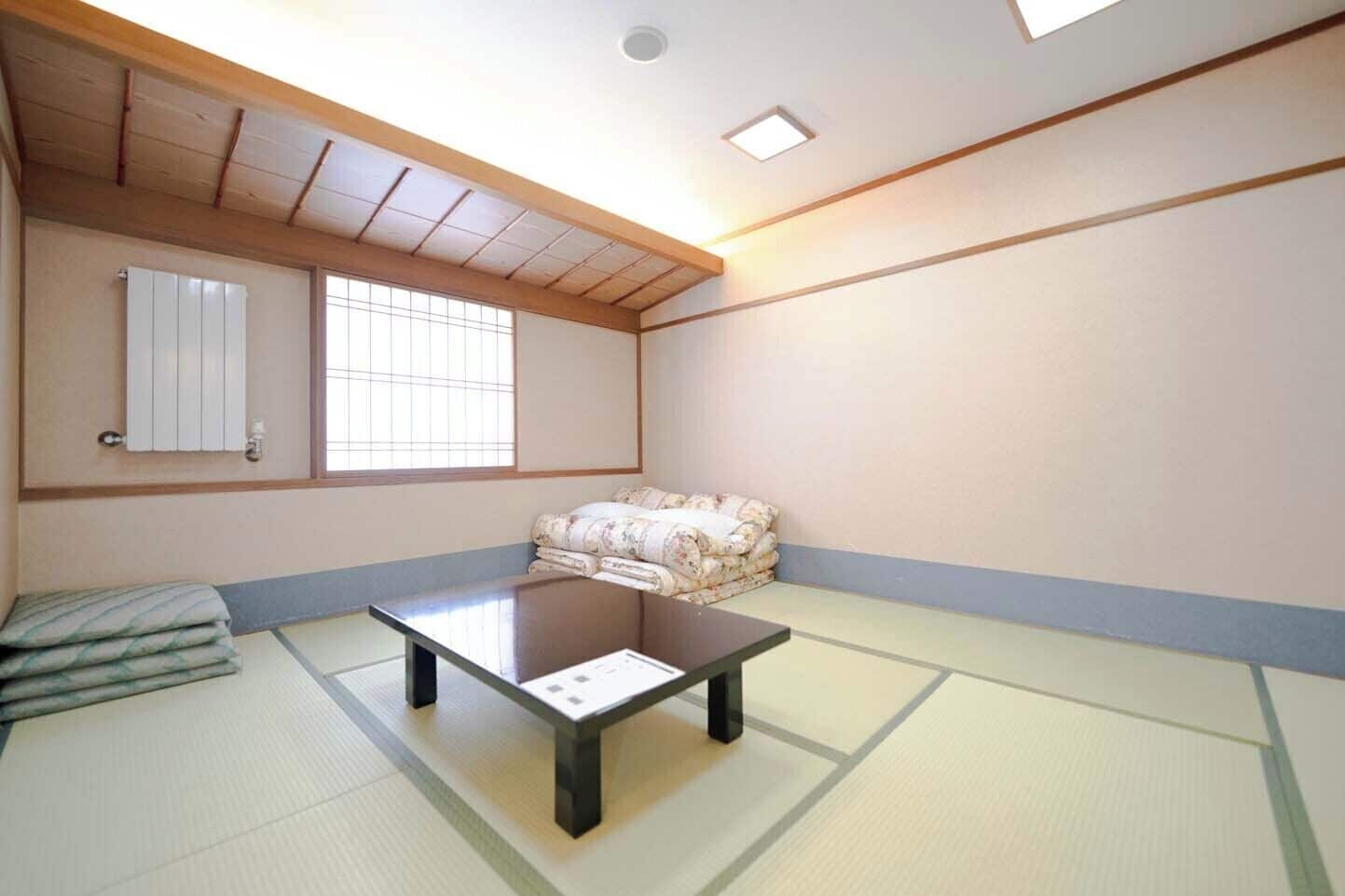 A tatami mat room with a low table, a futon bed, and a window with a grid pattern.