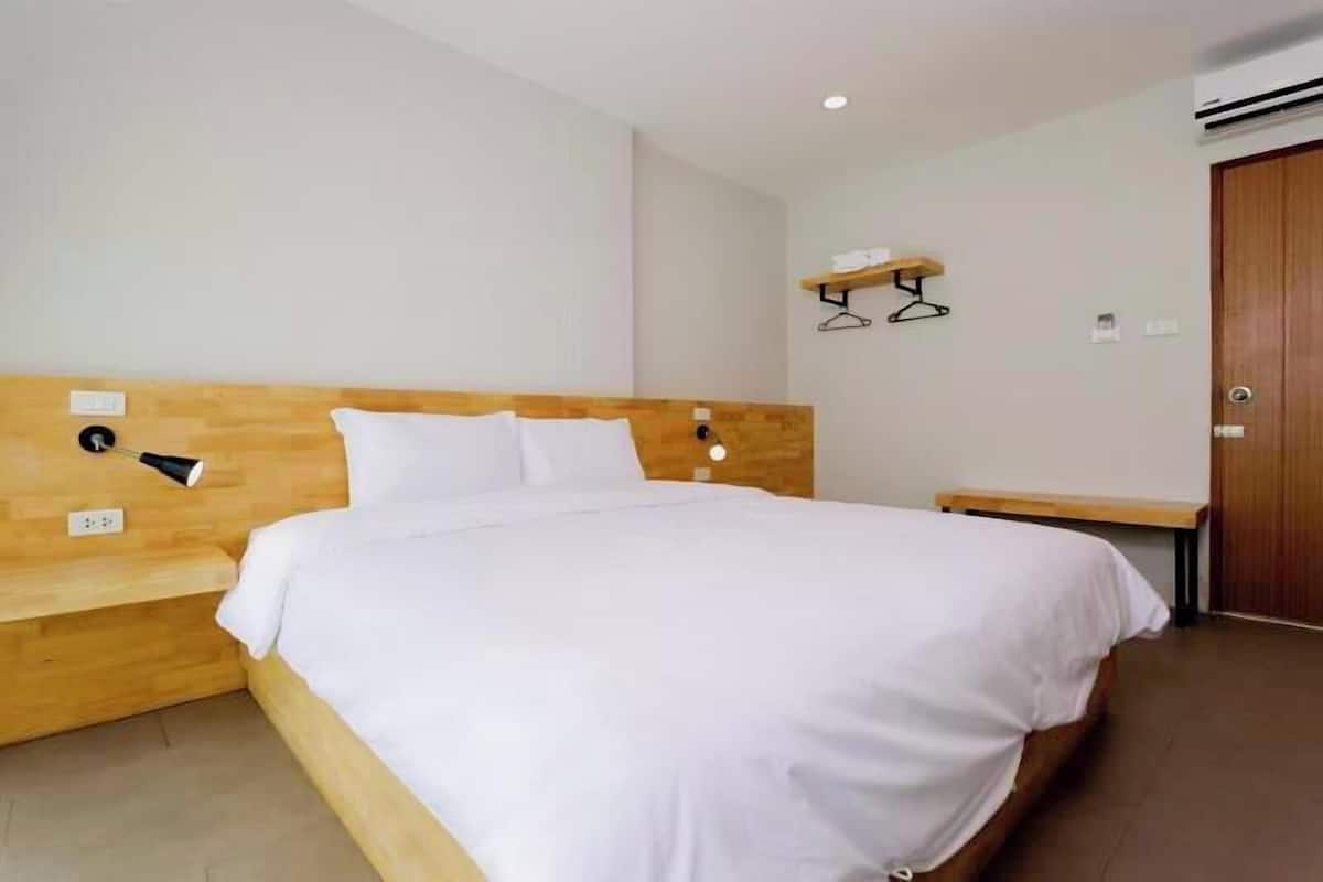 A neatly arranged hotel room with a wooden headboard, a single bed, a bedside table, a wall-mounted light, and a wooden bench.