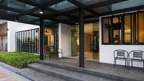 A modern building entrance with a glass facade, outdoor seating area, and steps leading to the entrance. - Easy Hotel (Lamphun)