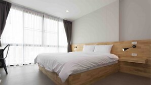 A modern hotel room with a wooden bed, a desk, and a large window with curtains. - Easy Hotel (Lamphun)