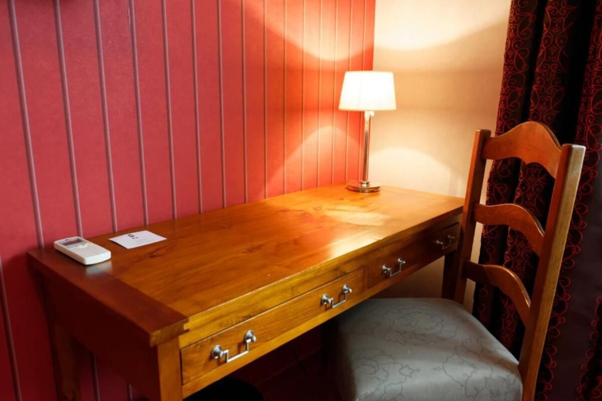 A wooden desk with drawers, a lamp, and a chair in a room with red walls.