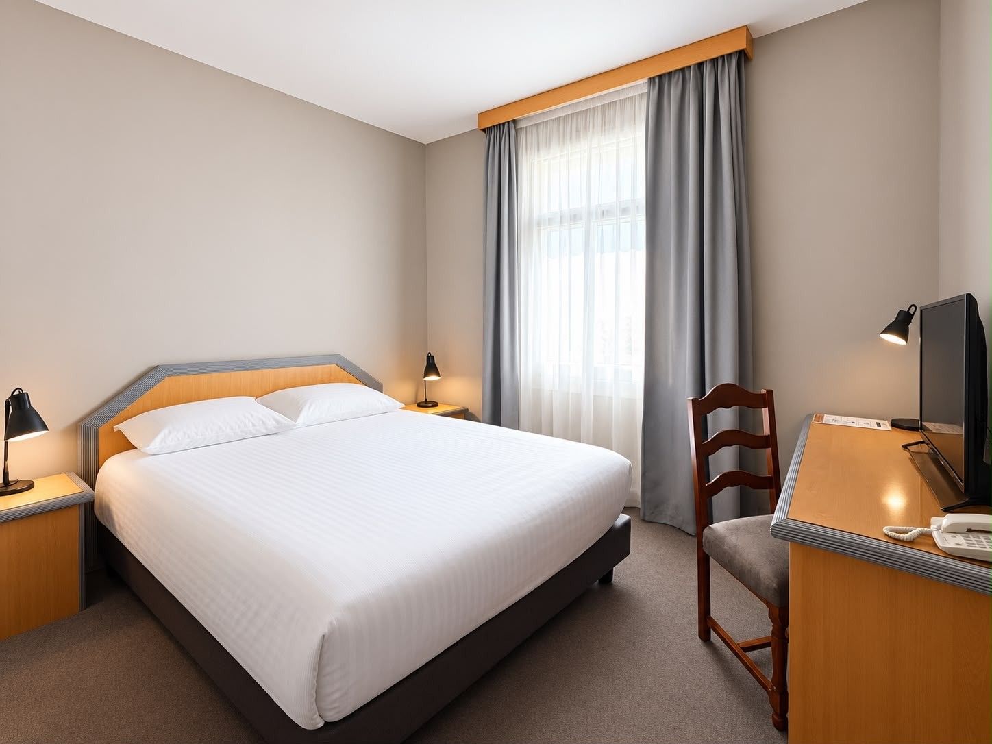 Une chambre d’hôtel comprenant un lit, un bureau avec une chaise, une télévision et un téléphone.