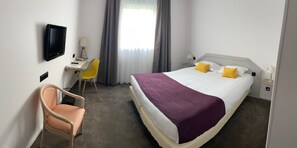 A hotel room with a bed, a desk, a chair, a TV, and a window with curtains. - Hotel Le Manoir (Orchies)