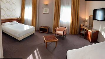 A hotel room with a bed, a desk, a chair, a small table, a television, and a mirror.