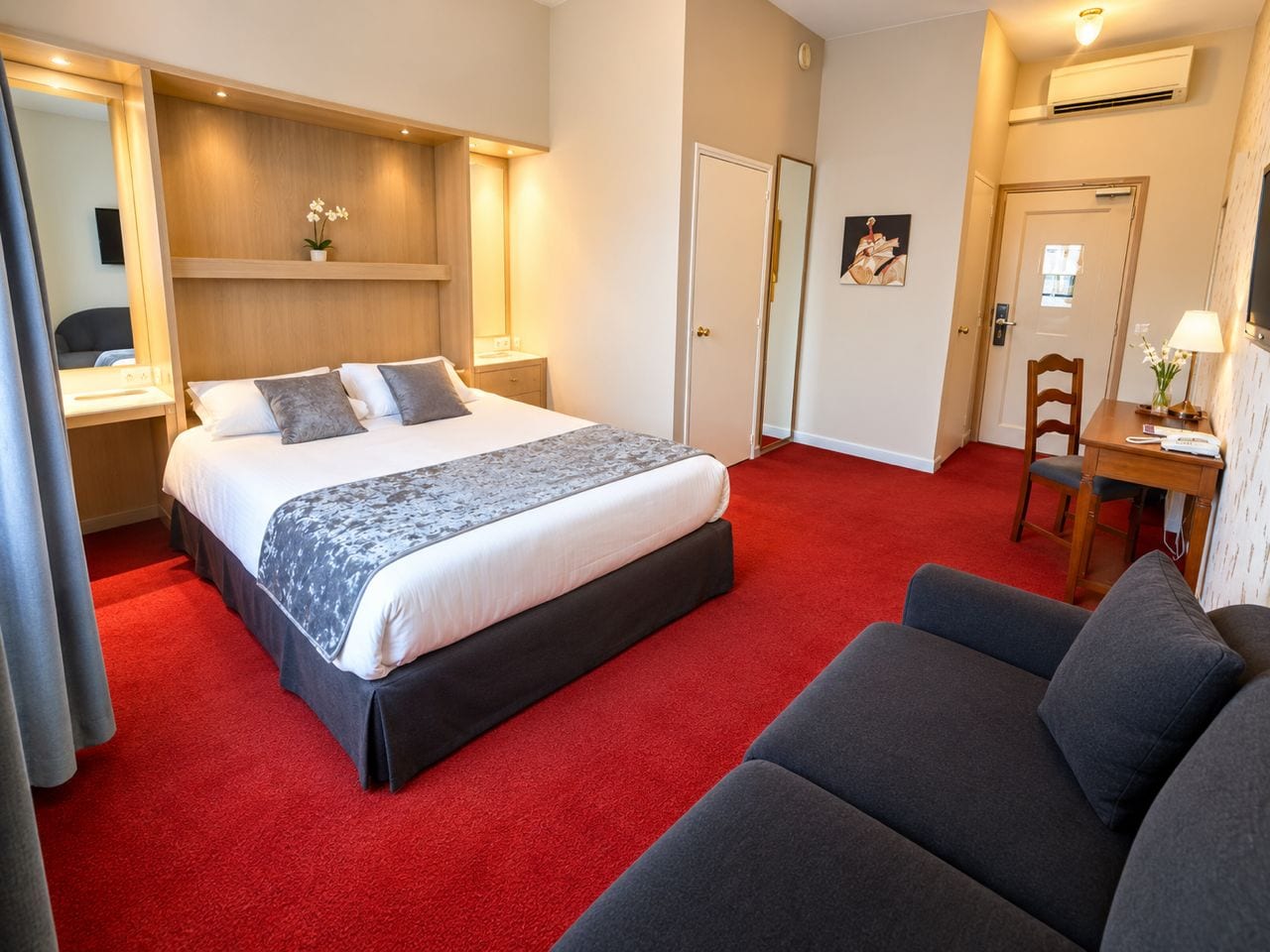 Una habitación de hotel con cama, sofá, escritorio y espejo.