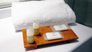 Una bandeja de madera con tres pastillas de jabón blancas y dos botellas de loción sobre una superficie blanca, con una toalla blanca al fondo.