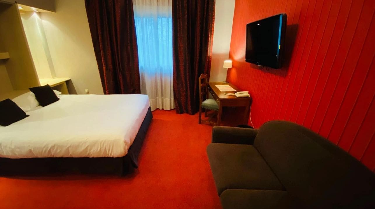 A hotel room with a bed, a desk, a chair, a television, and a window with curtains.