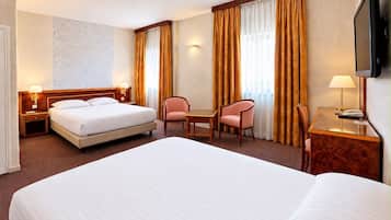 Une chambre d’hôtel avec un grand lit, un bureau, deux chaises, une télévision et une lampe fixée au mur.