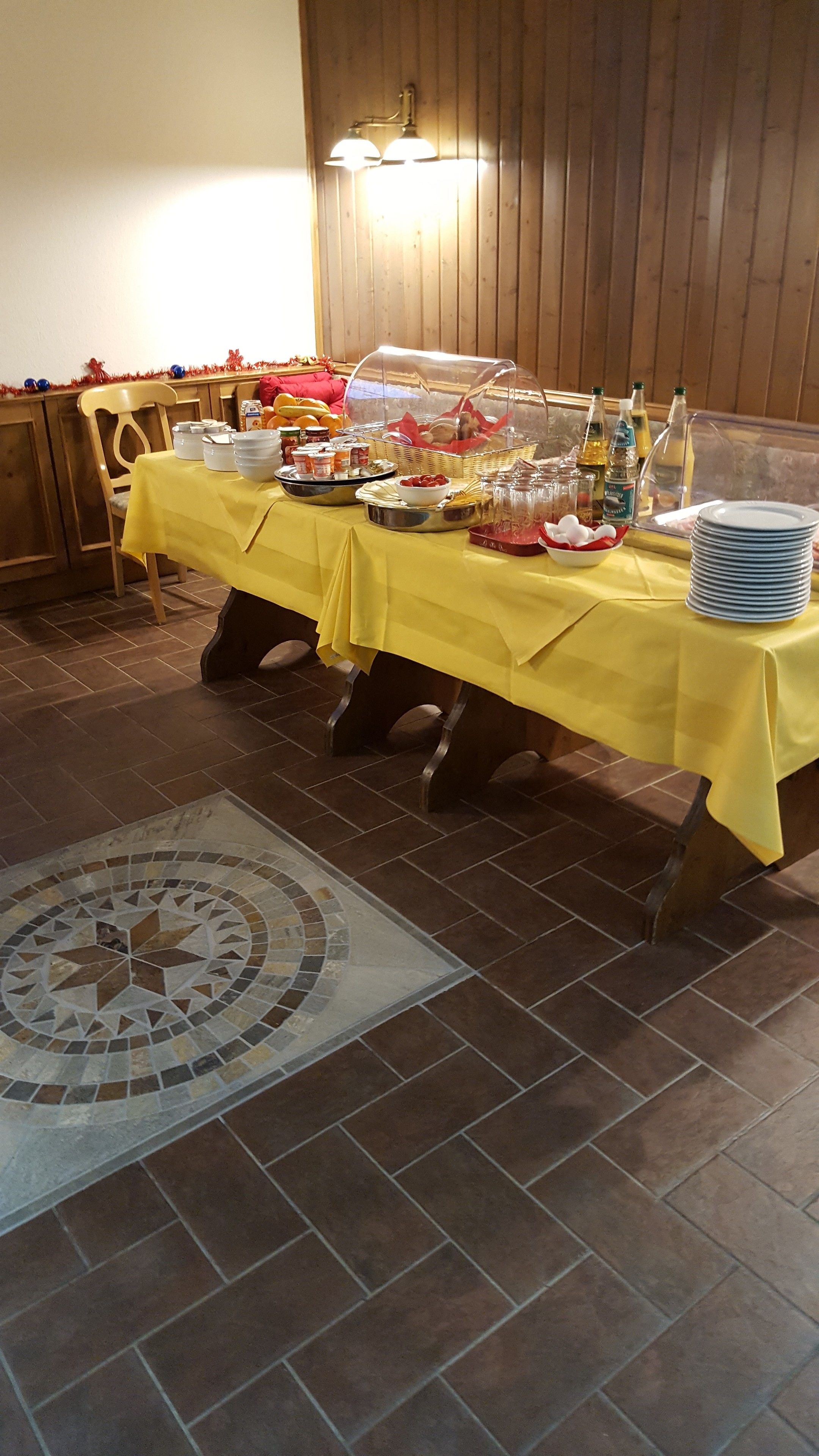A buffet table with a yellow tablecloth, covered with a glass dome, and various food items and condiments.