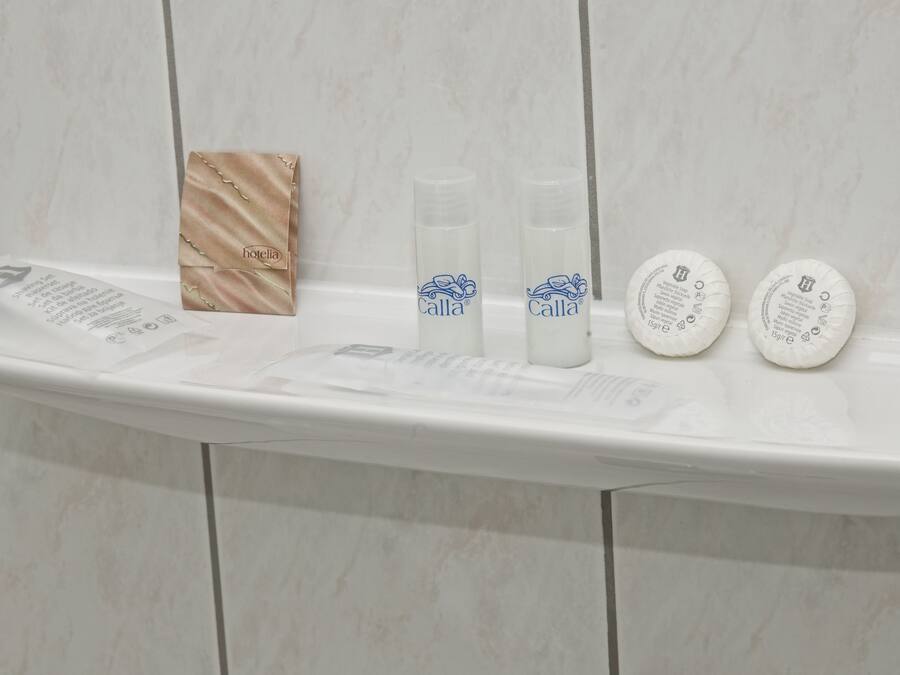 A bathroom shelf with toiletries including a tissue box, two bottles of Calla brand lotion, and two round soap bars.
