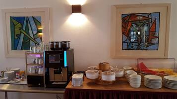 A breakfast buffet setup with a coffee machine, plates, bowls, and glasses.