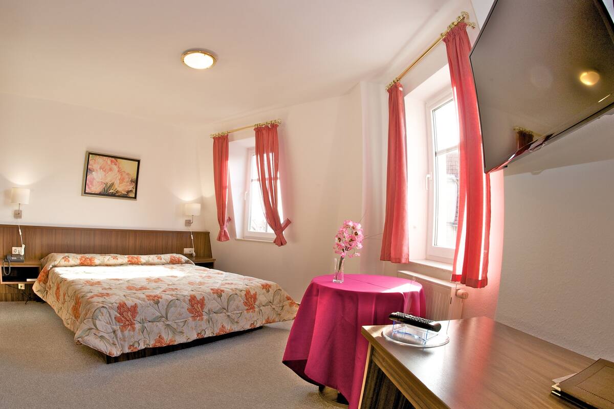 A hotel room with a bed, bedside table, lamp, and a window with curtains.