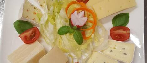 A plate with various cheeses, tomatoes, lettuce, and basil leaves arranged on a white plate.