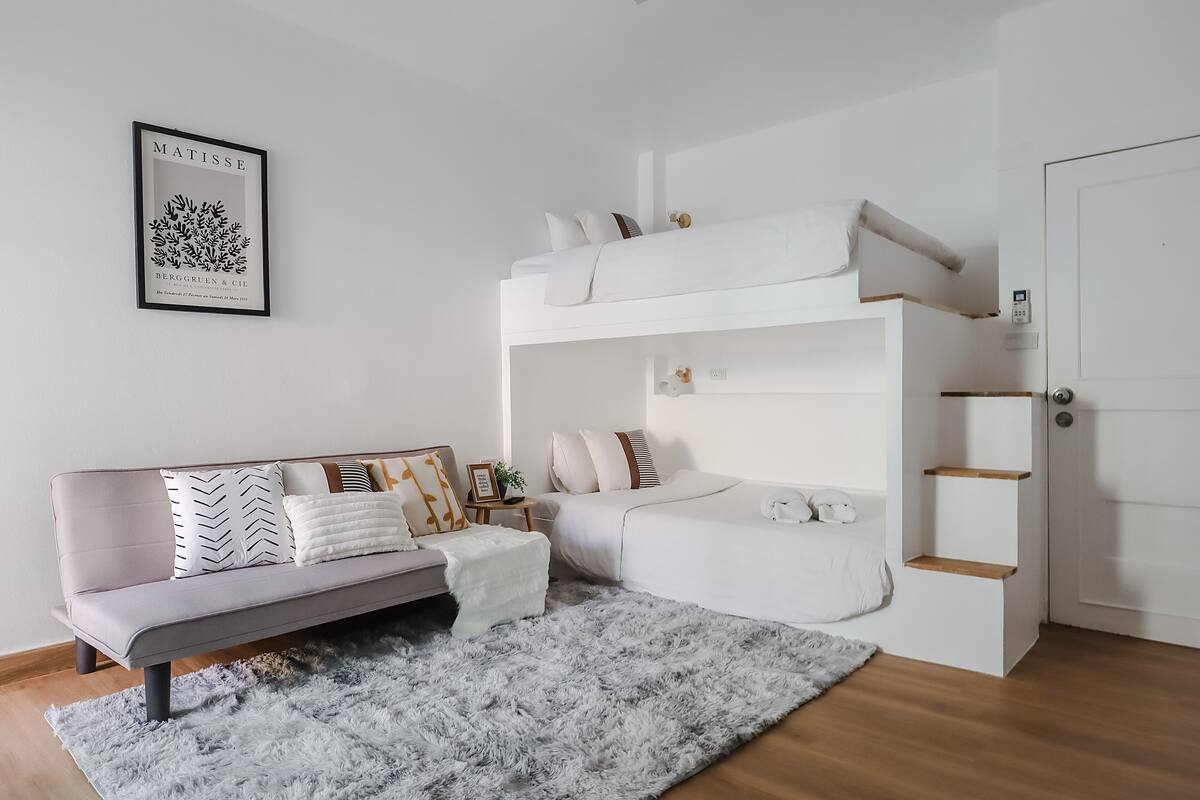 A modern, minimalist bedroom with a bunk bed, a sofa, and a gray furry rug.