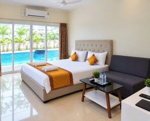 A hotel room with a bed, a sofa, a table with amenities, and a view of a swimming pool. - Hotel Dolphin (Kanthi)