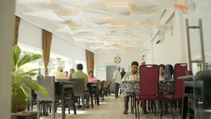A restaurant with a modern ceiling design, tables, chairs, and a potted plant. - Hotel Dolphin (Kanthi)