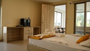 A hotel room with a bed, a desk, a television, and a balcony with a view of palm trees. - Hotel Dolphin (Kanthi)