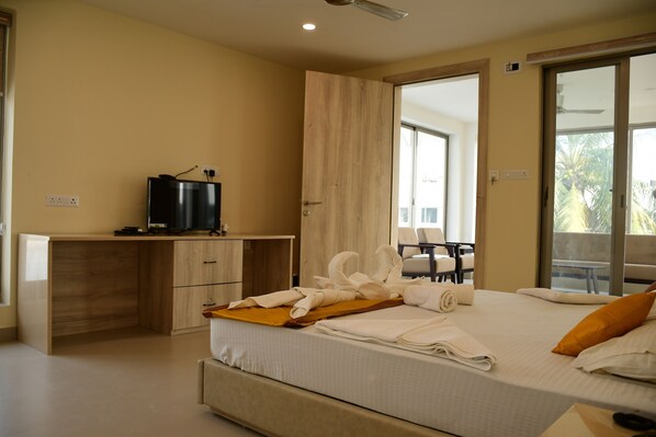 A hotel room with a bed, a desk, a television, and a balcony with a view of palm trees. - Hotel Dolphin (Kanthi)