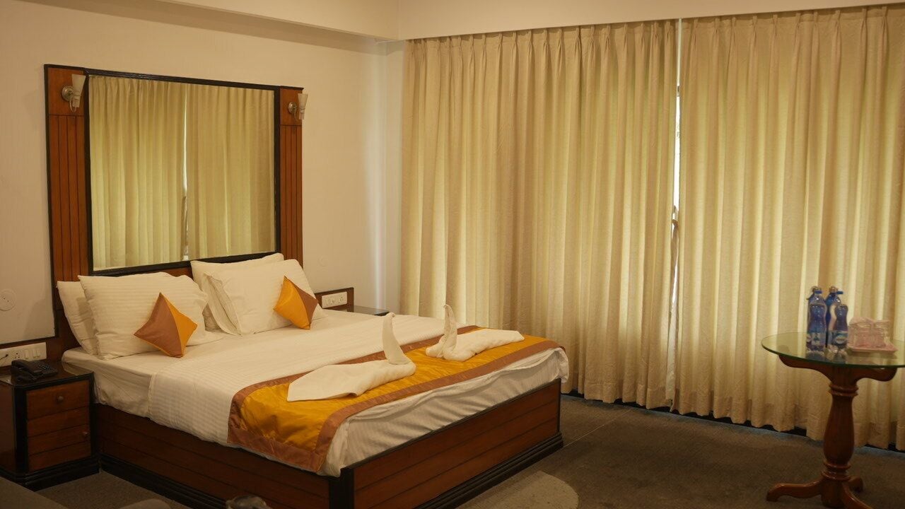 Ein Hotelzimmer mit einem großen Bett, einem Nachttisch, Vorhängen und einem Fenster.
