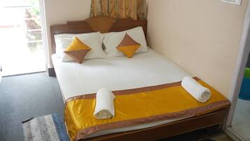 Una cama bien hecha con una colcha amarilla y marrón, dos almohadas y dos toallas enrolladas.