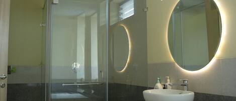 A modern bathroom with a glass shower enclosure, a round mirror, and a white sink.