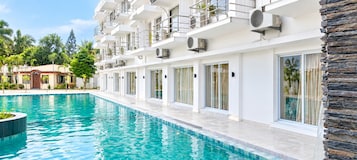 A modern hotel with a swimming pool, balconies, and air conditioning units.