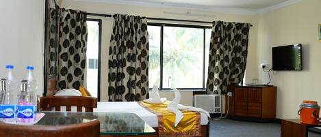 Ein Hotelzimmer mit Bett, Fernseher, Schreibtisch mit Stuhl, Tisch und einem Fenster mit Vorhängen.