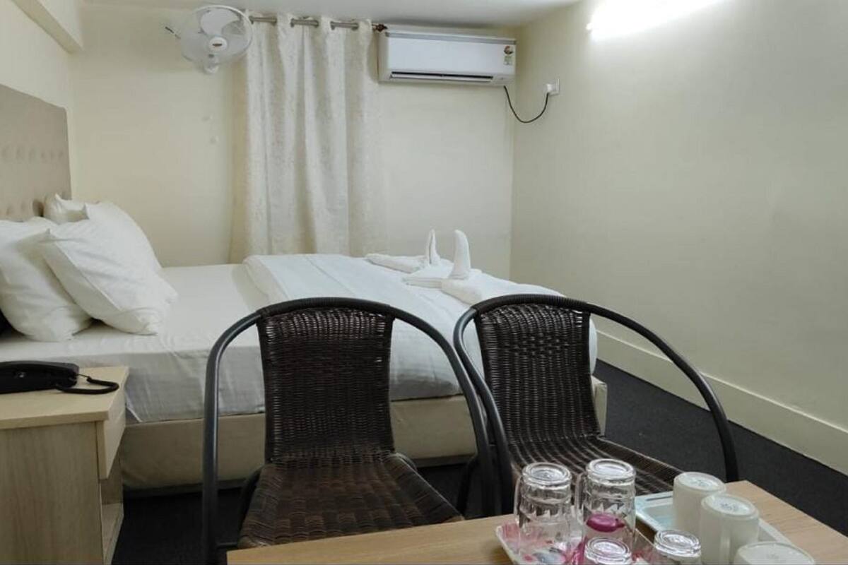 Ein kleines Hotelzimmer mit einem Einzelbett, zwei Stühlen, einem Tisch mit Pflegeprodukten, einem Nachttisch mit Telefon und einer Klimaanlage.
