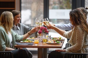 Un grupo de personas brindando en una mesa con copas de vino, rodeado de platos de comida y un jarrón de flores.