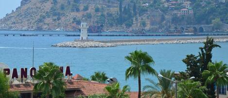 Un pueblo costero con un faro destacado, un muelle que se adentra en el mar y un edificio con el rótulo 'PANORAMA'.