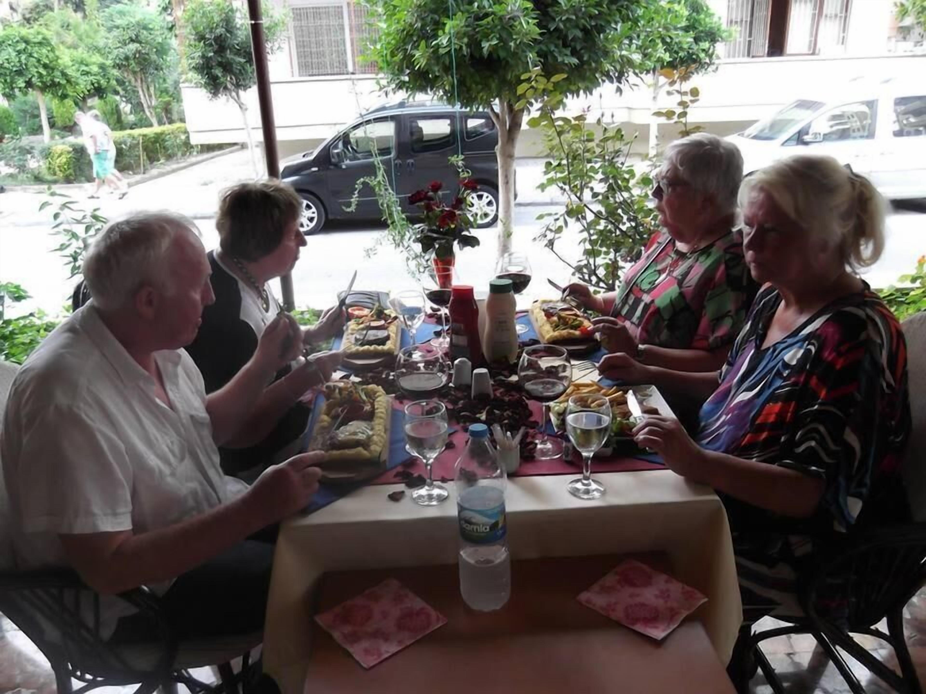 A group of people dining at an outdoor table with various dishes and drinks.