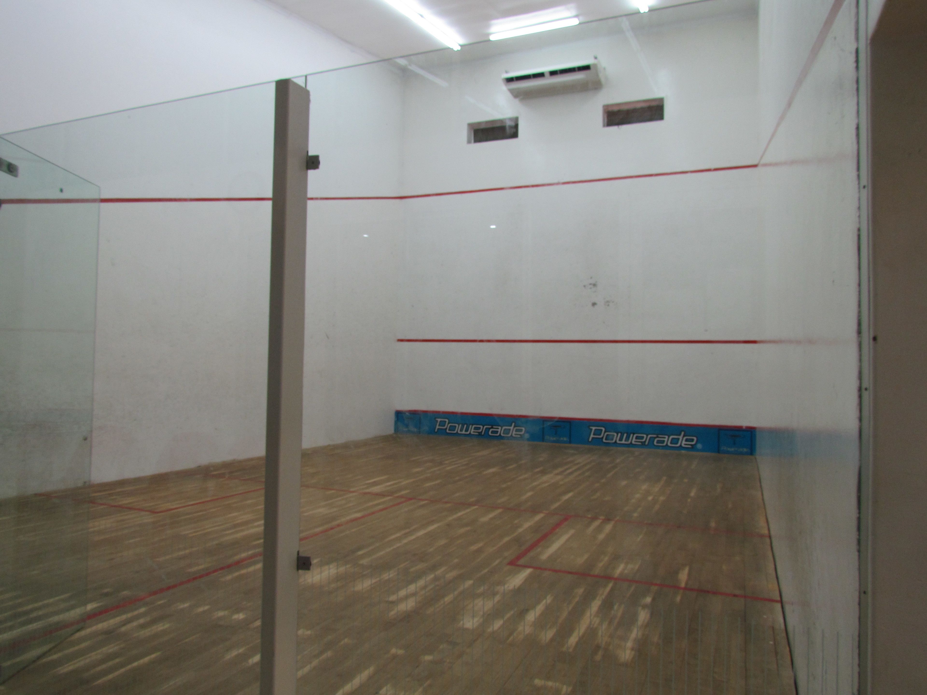 A squash court with a wooden floor, white walls, and red boundary lines.