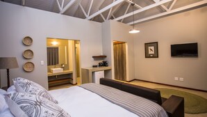 A modern hotel room with a large bed, a desk with a sink, a television, and a ceiling with exposed beams.