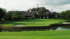 A golf course with a clubhouse featuring multiple chimneys and a pond.