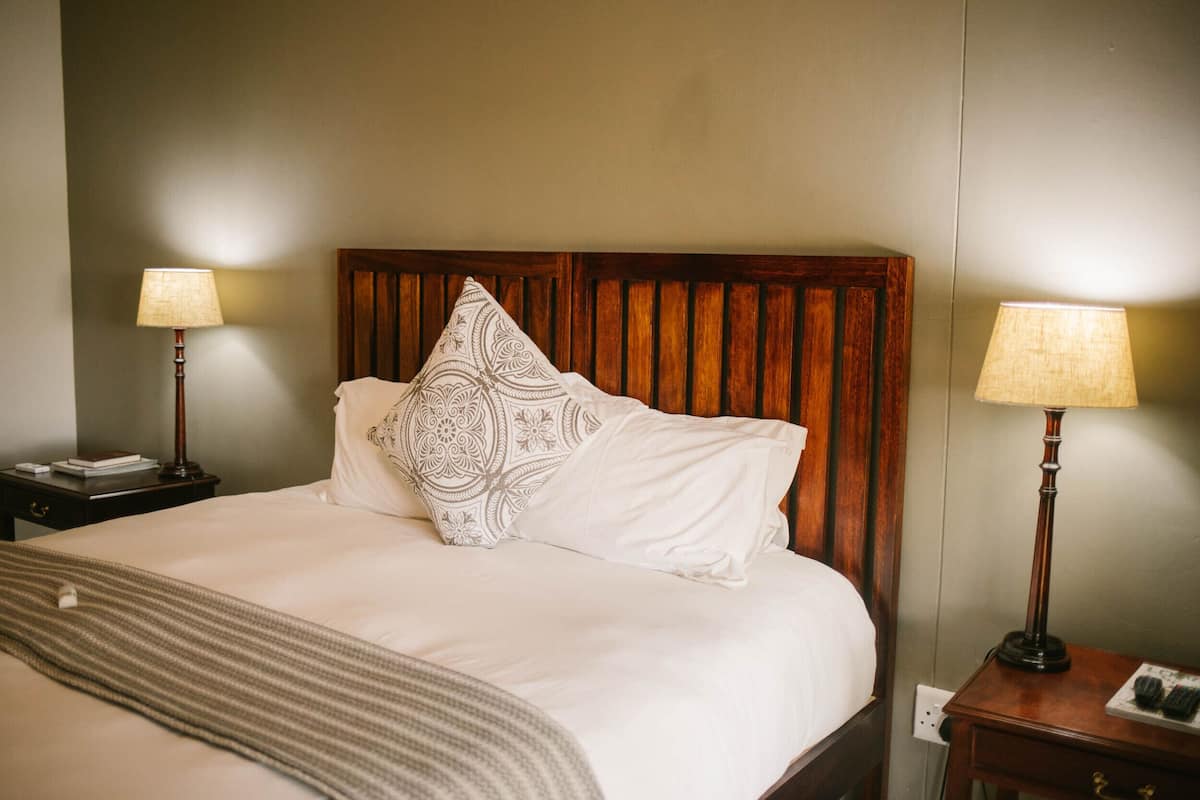 Un lit bien fait, agrémenté d’un coussin à motifs, d’une tête de lit en bois et de deux lampes de chevet.