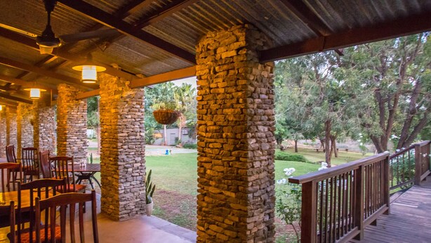 A covered outdoor dining area with stone pillars, wooden tables, and chairs.