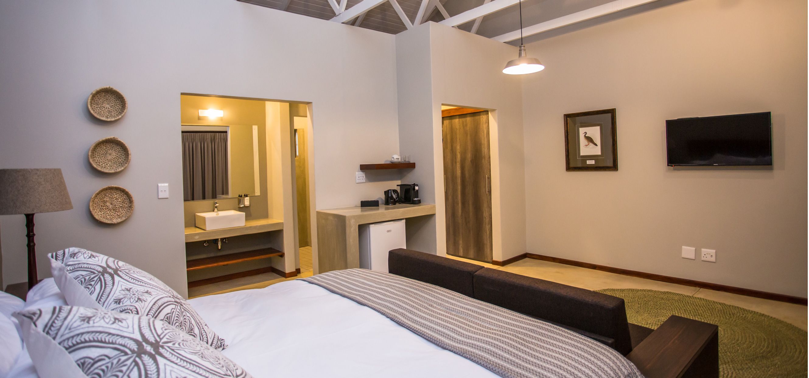 A hotel room with a bed, a desk, a mirror, a television, and a bathroom visible through an open door.