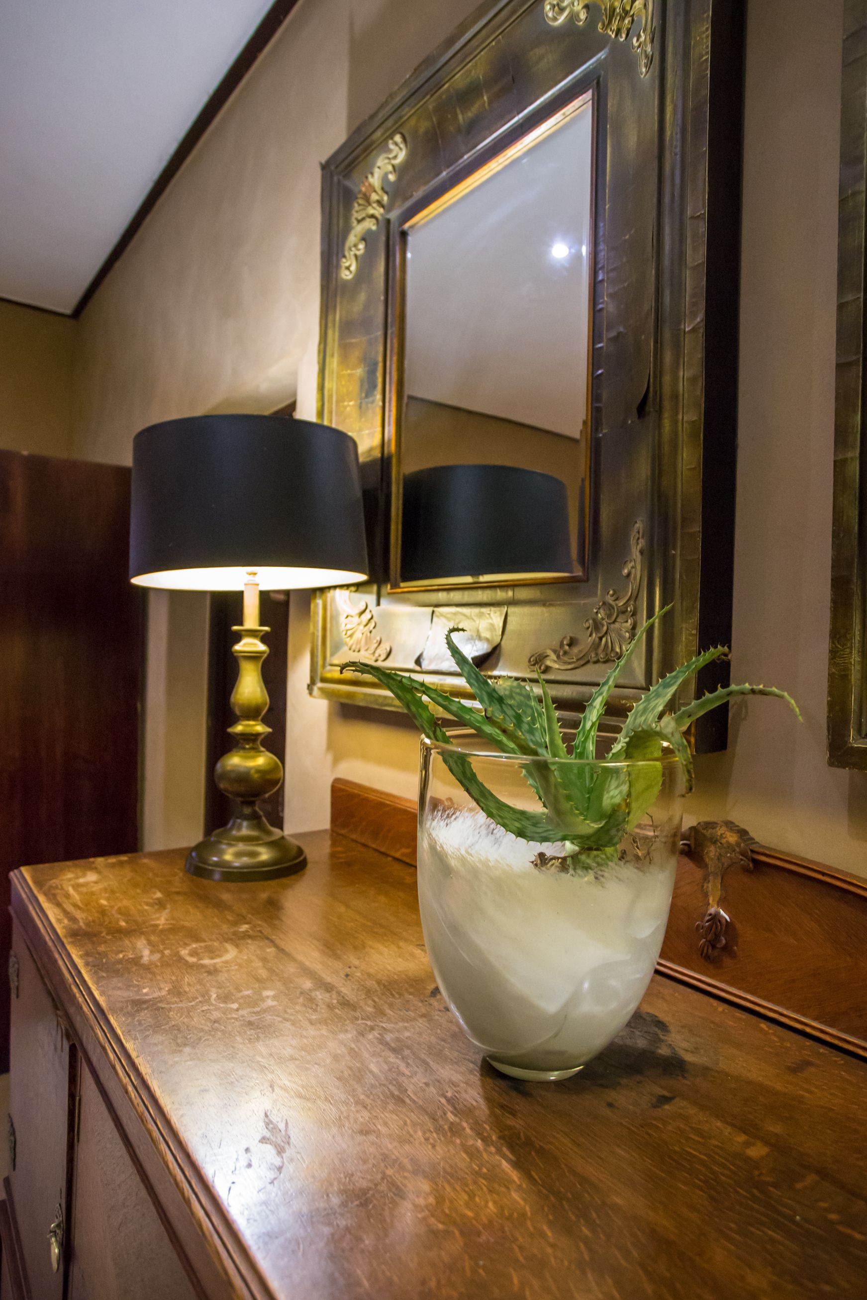 A wooden dresser with a lamp and a glass vase containing a plant.