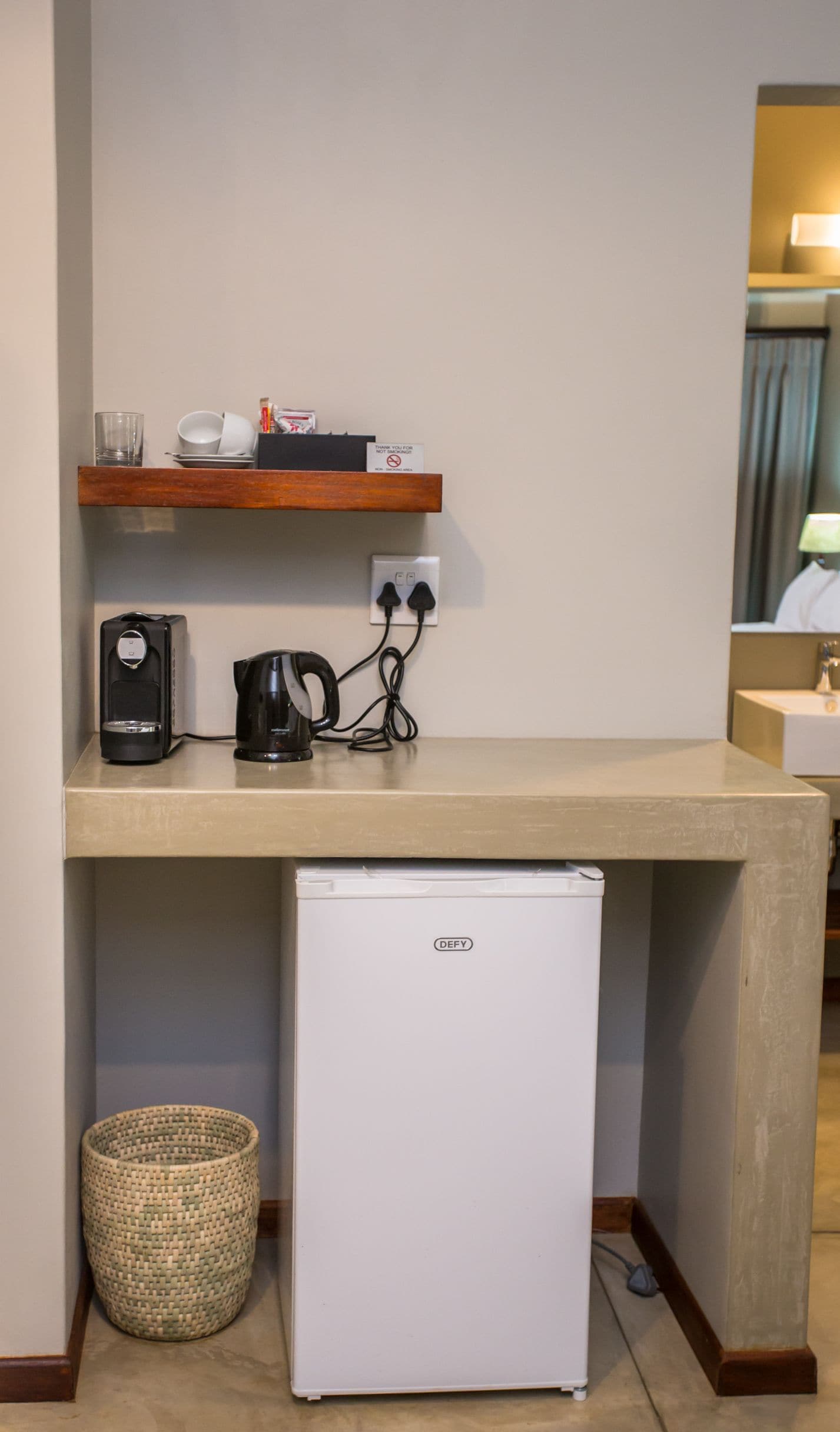 A compact kitchenette with a coffee maker, kettle, and a small refrigerator.