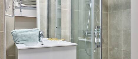 Un baño moderno con ducha envuelta en vidrio, un lavamanos blanco con una toalla y un espejo sobre el lavamanos.