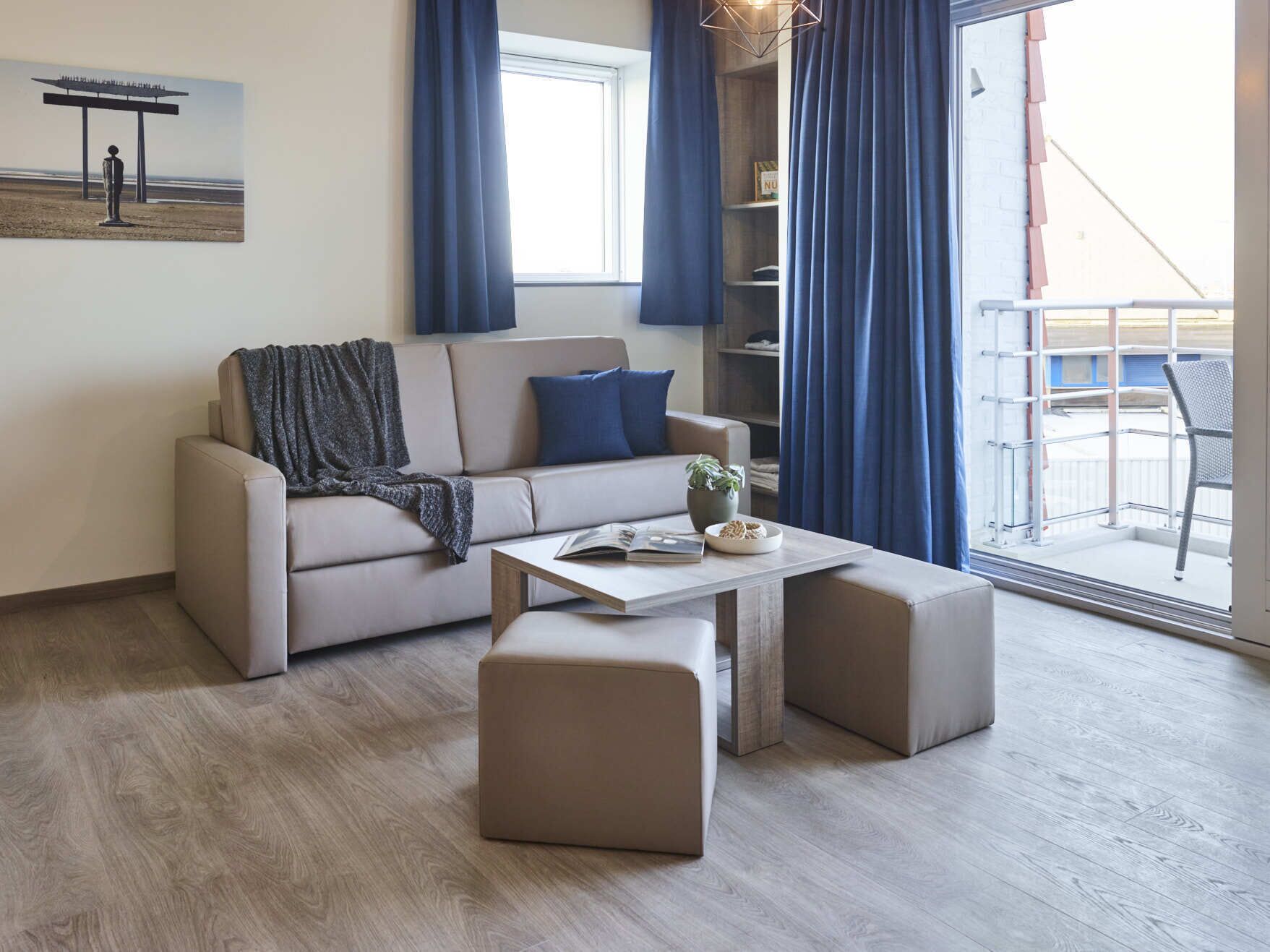 Ein modernes Wohnzimmer mit einer Couch, einem Hocker und einem Couchtisch. Ein Bücherregal und ein Fenster mit Vorhängen sind ebenfalls vorhanden.