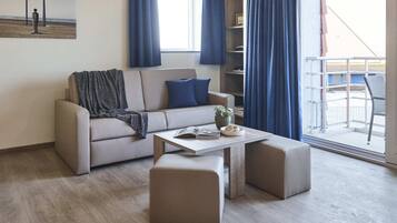 A modern living room with a sofa, ottoman, and a coffee table. There is a bookshelf and a window with curtains.