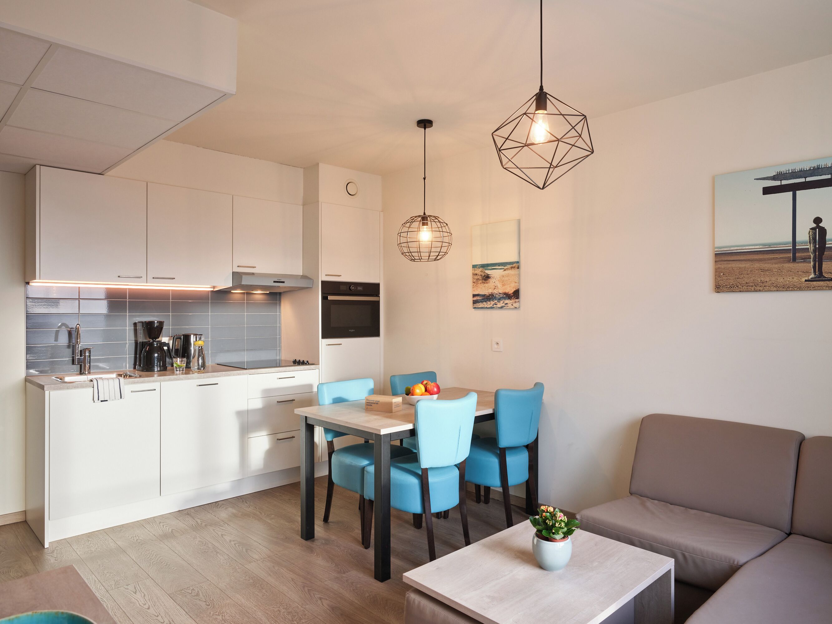 Een moderne keuken met witte kasten, een eethoek met blauwe stoelen en een beige bank.