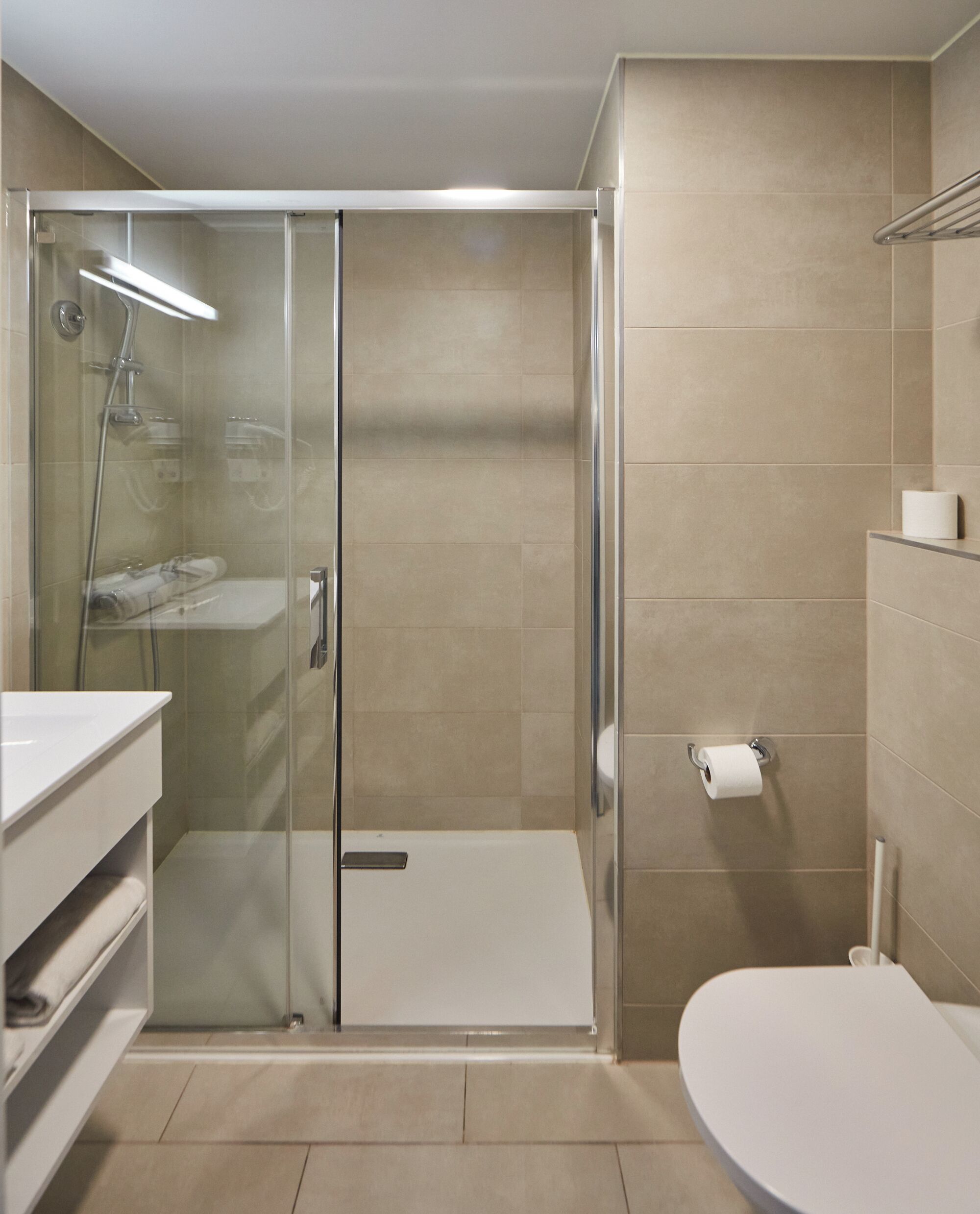 Een moderne badkamer met een douche met glazen wand, een toilet en een wastafel.