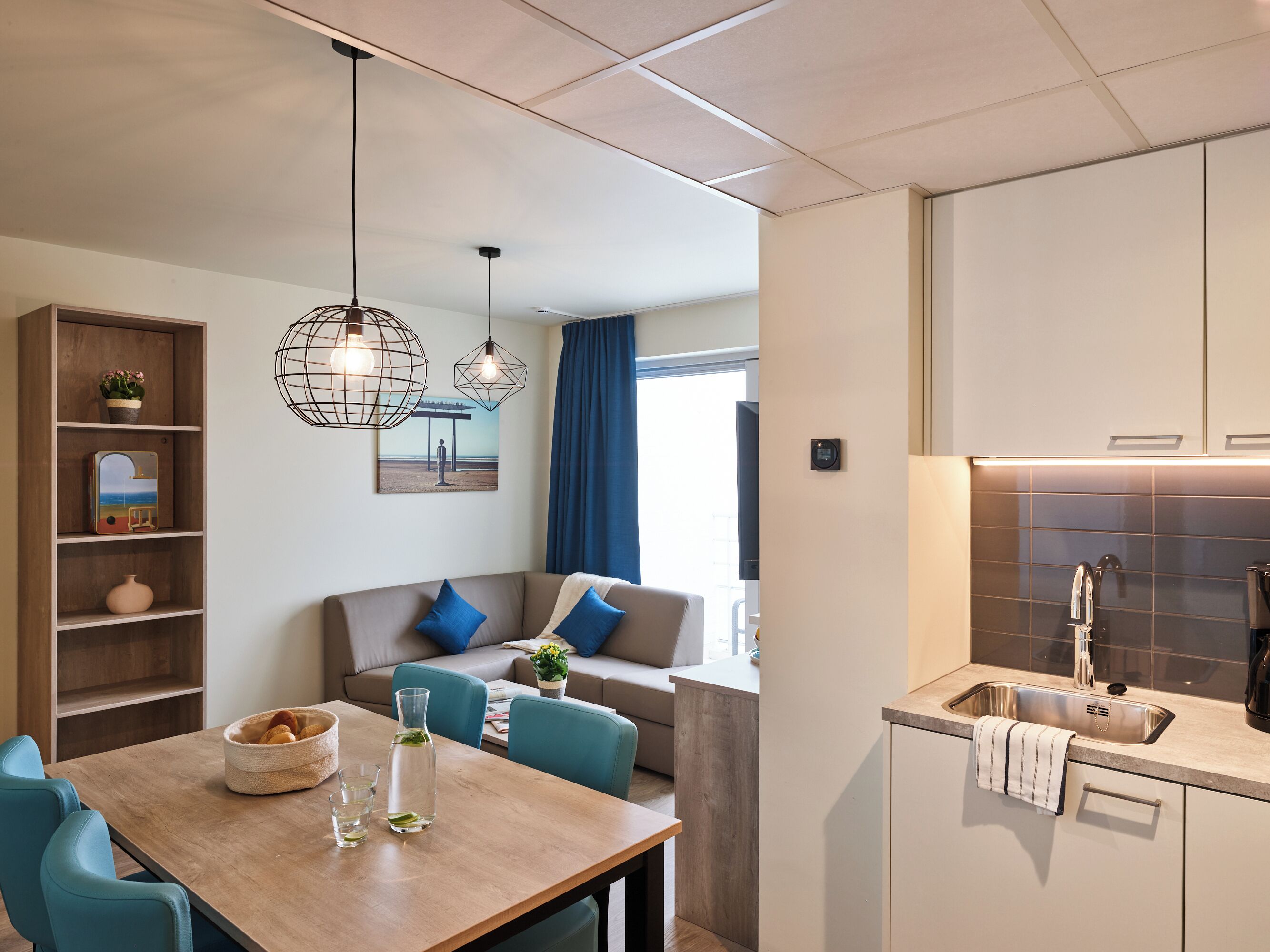 A modern kitchen with a built-in sink, a dining area with a wooden table, and a seating area with a sofa and chairs.
