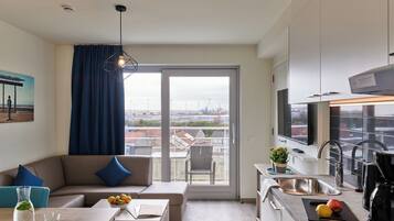 Un apartamento moderno con sala de estar, kitchenette y un amplio ventanal corredera al balcón.