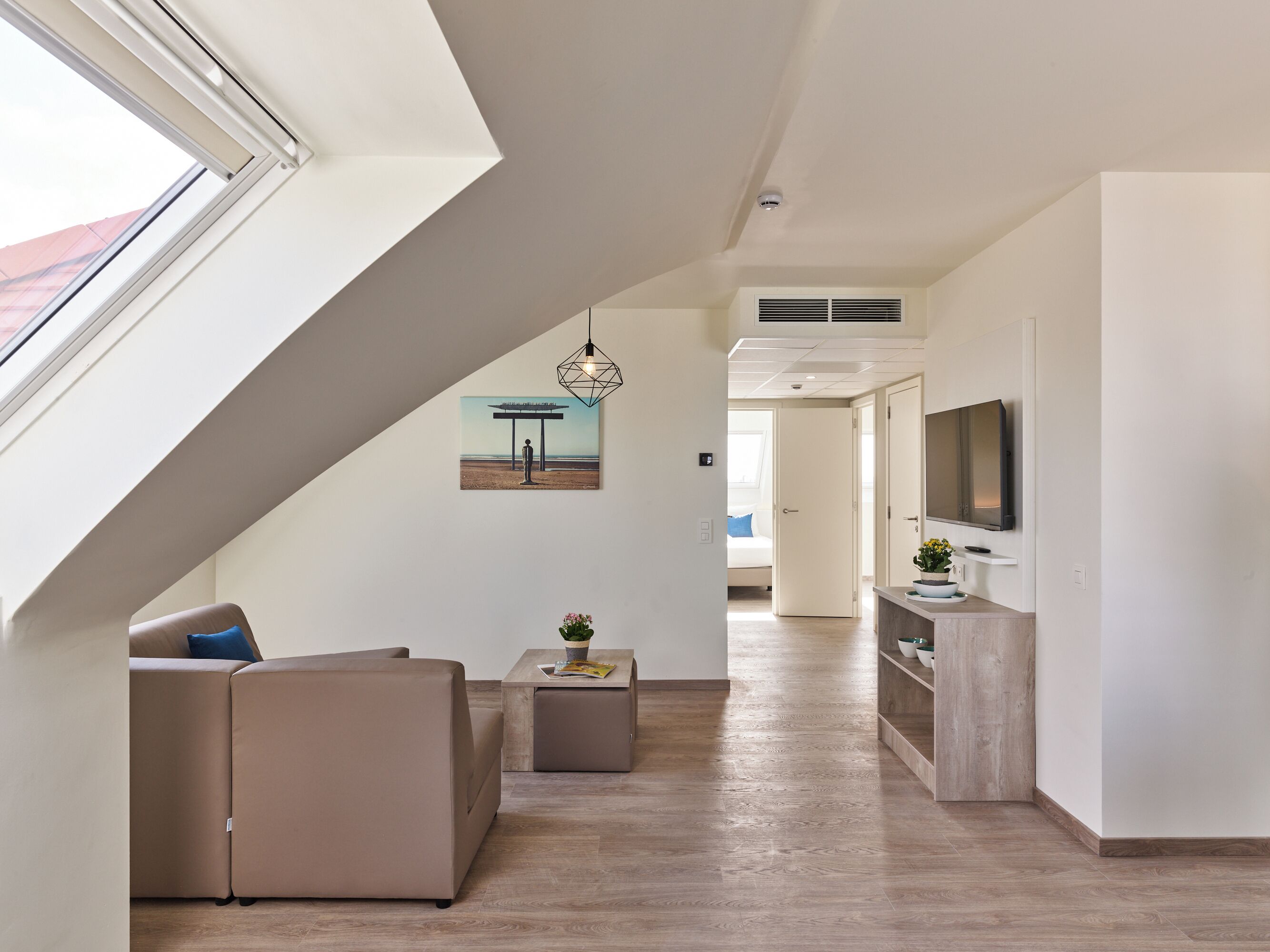 Un salon moderne avec un canapé, une table basse et un téléviseur. Un tableau orne le mur et une fenêtre laisse entrer la lumière naturelle.