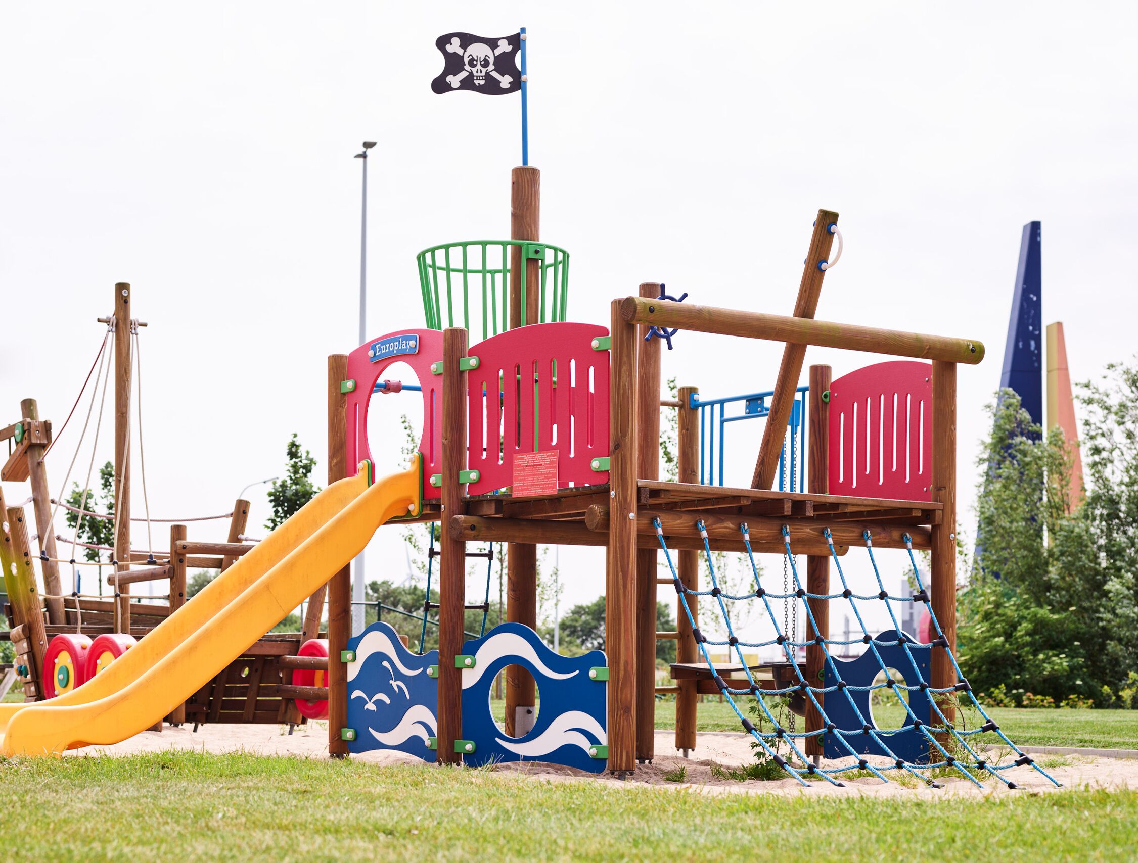 A playground with a slide, climbing net, and a pirate flag.
