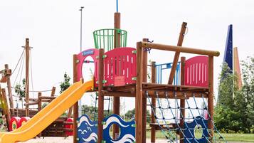 A playground with a slide, climbing net, and a pirate flag.